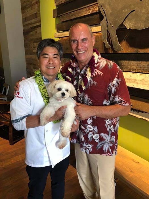 2 men holding a white dog and standing for the photograph