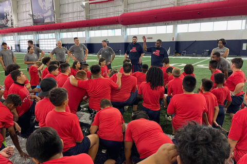 children wearing Red color t-shirt in the stadium and some coaches explaining them