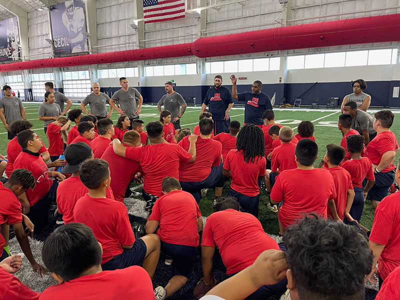 children wearing Red color t-shirt in the stadium and some coaches explaining them