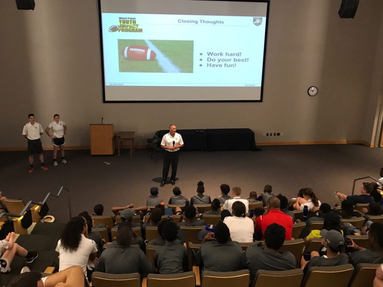 Man speaking in the webinar and people sitting in the hall