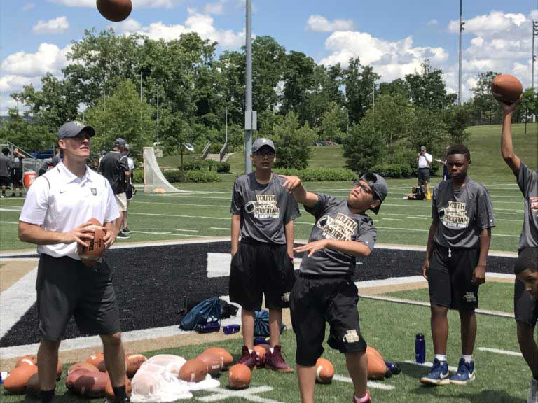 Boy throw a ball and coach is beside and other players are around the ground