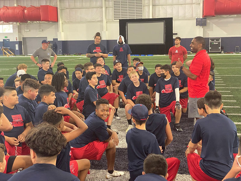 children wearing dark blue color t-shirt in the stadium and some coaches explaining them