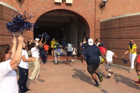 students running into the M entrance gate with cheer leader cheering them