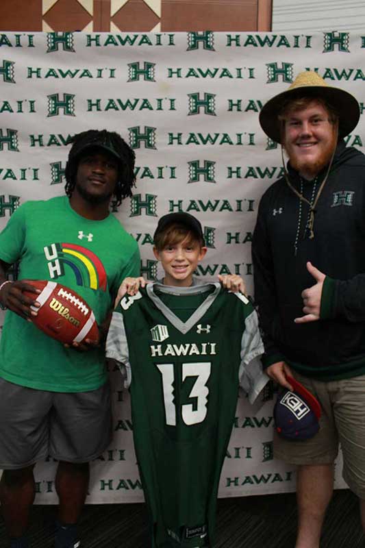 Boy holding a black jersey standing with his instructors