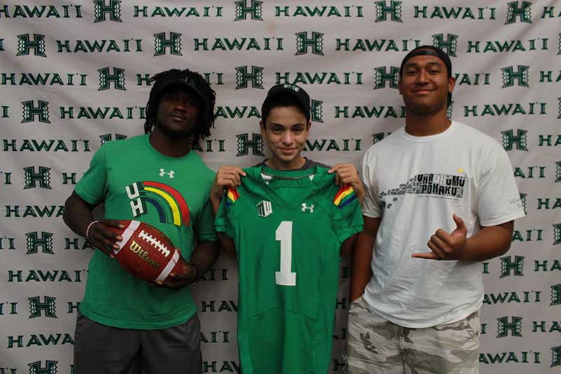 Boy holding a green jersey standing with his instructors