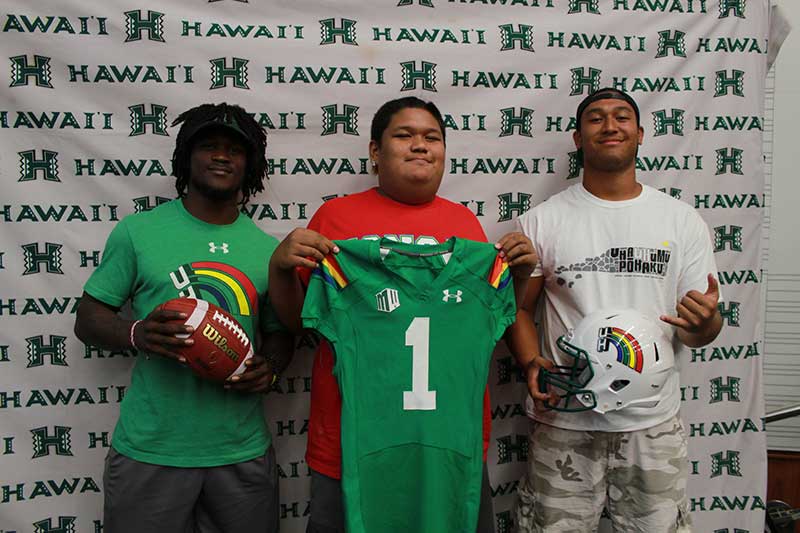 Boy holding a green jersey standing with his instructors