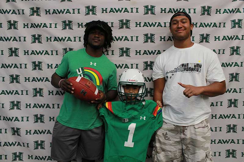 Boy holding a green jersey and wearing helmet standing with his instructors