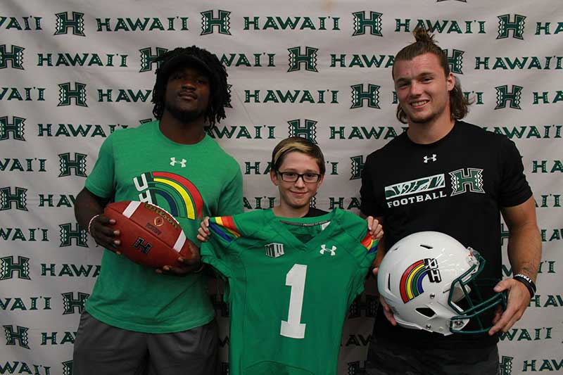 Boy holding a green jersey standing with his instructors