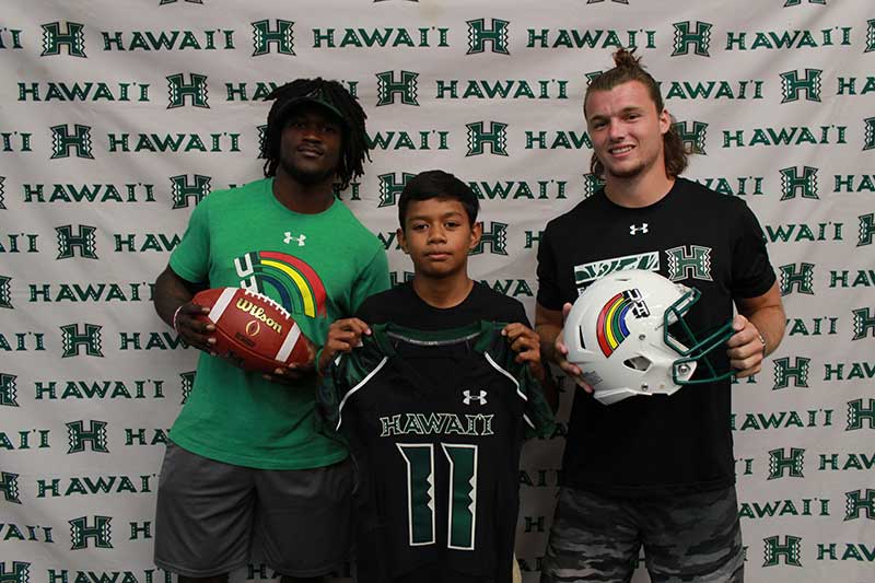 Boy holding a black jersey standing with his instructors