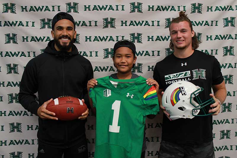 Boy holding a green jersey standing with his instructors