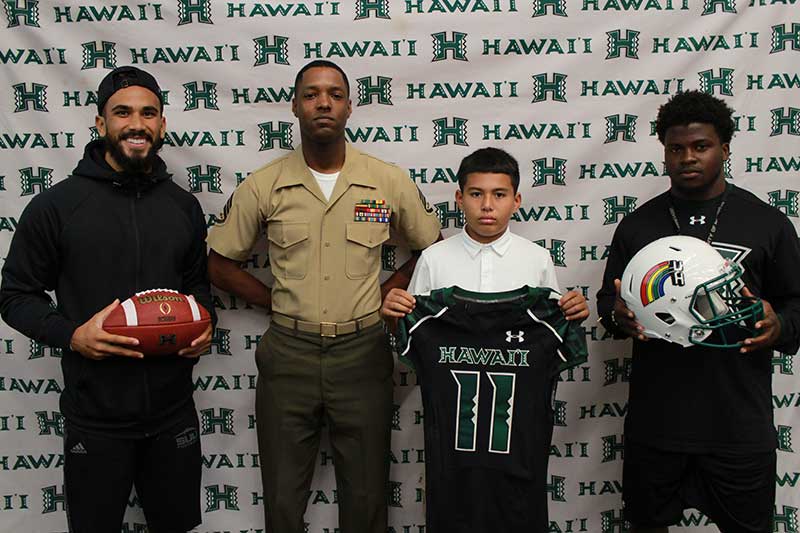 Boy holding a black jersey standing with his instructors