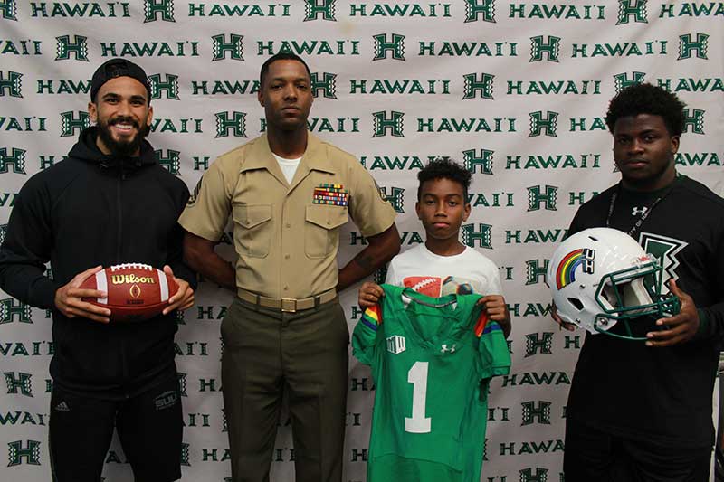 Boy holding a green jersey standing with his instructors