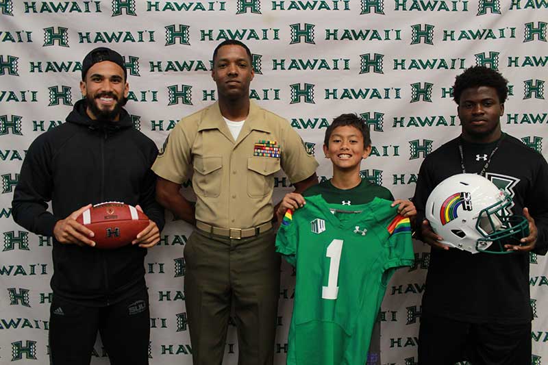 Boy holding a green jersey standing with his instructors